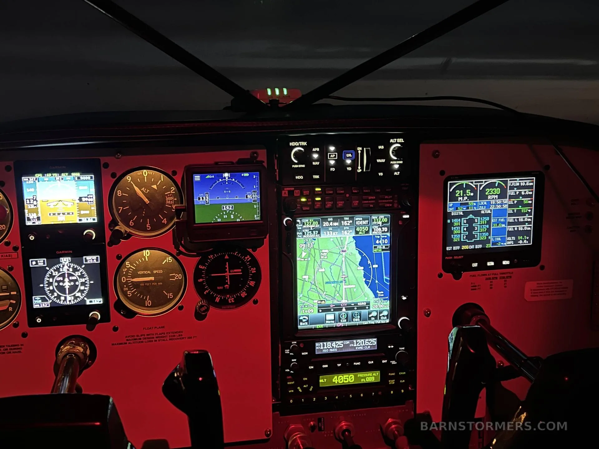 The illuminated cockpit instrument panel of an aircraft, showing various gauges and digital displays with a red glow.