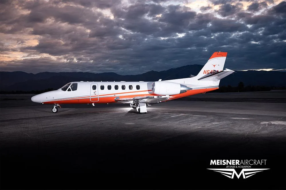 A white and orange Cessna Citation Excel (N648AJ) parked on an airfield at dusk, viewed from a slightly different angle.