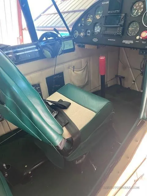 The interior of an aircraft cabin, showing a green and beige seat and part of the cockpit panel.