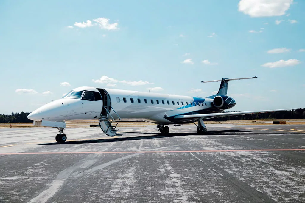 A white and blue Embraer ERJ 145 regional jet with its passenger door open and stairs deployed, parked on an airport tarmac.