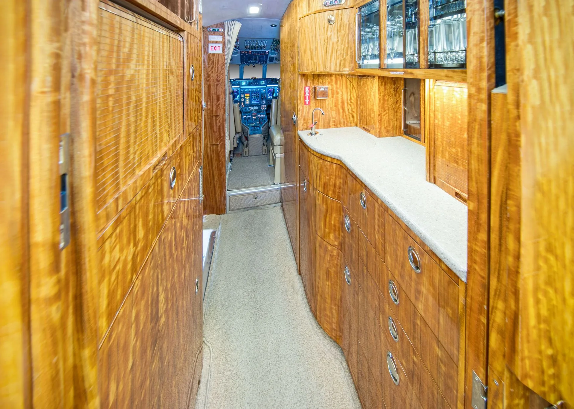 A view of the aircraft's galley area with wood paneling, a sink, and the cockpit visible down the aisle.