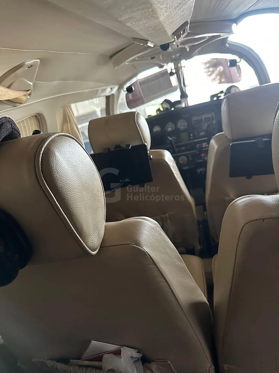 A close-up view of the tan leather passenger seats in a small aircraft cabin, looking towards the cockpit.