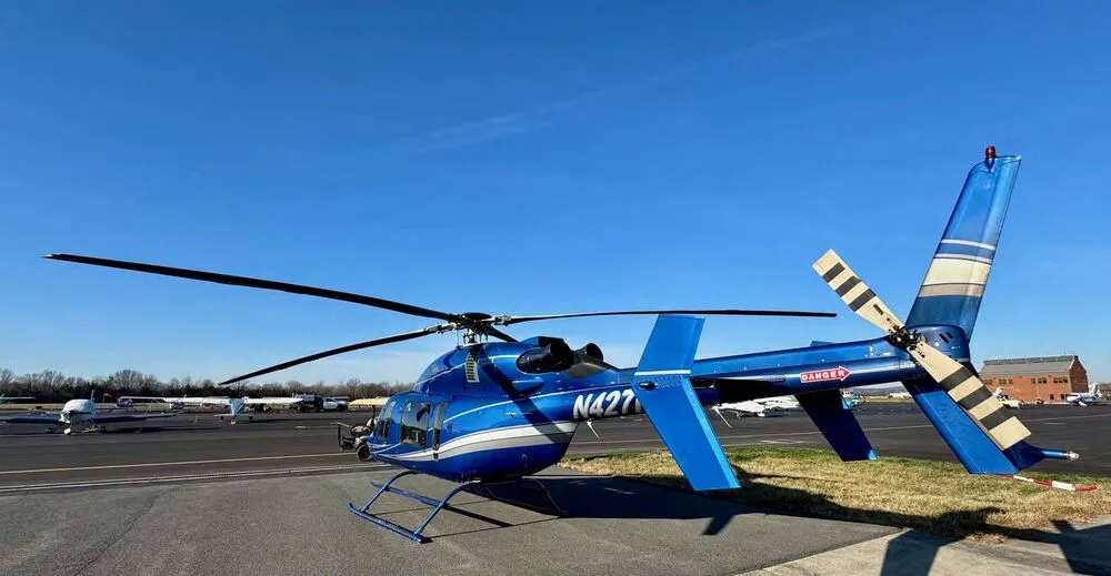 A rear-side view of a blue Bell 427 helicopter with white and silver stripes parked on an airfield.