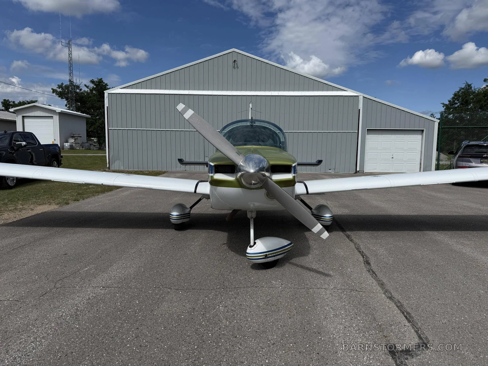 A front view of a Grumman American aircraft with a two-blade propeller, parked in front of a hangar.