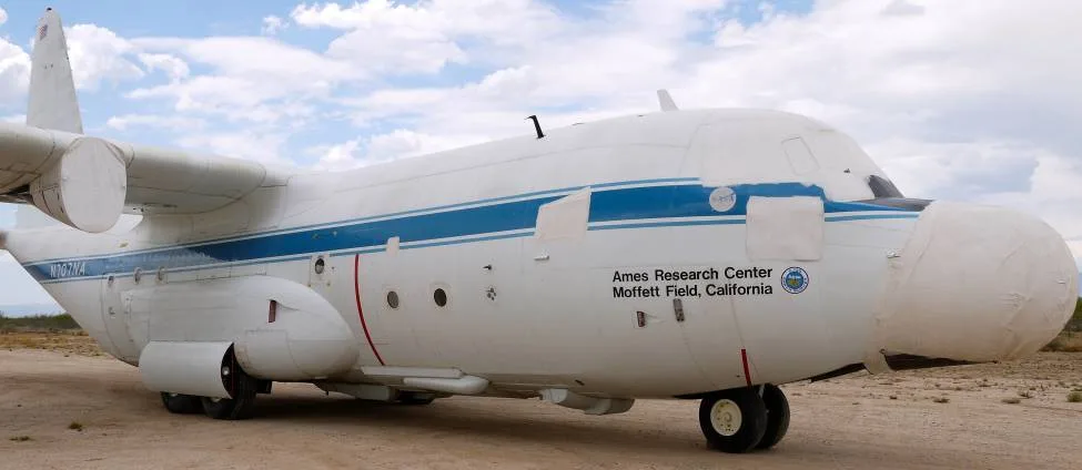 The front-left side of a white NASA C-130 aircraft with covered nose and engine inlets in a desert boneyard.