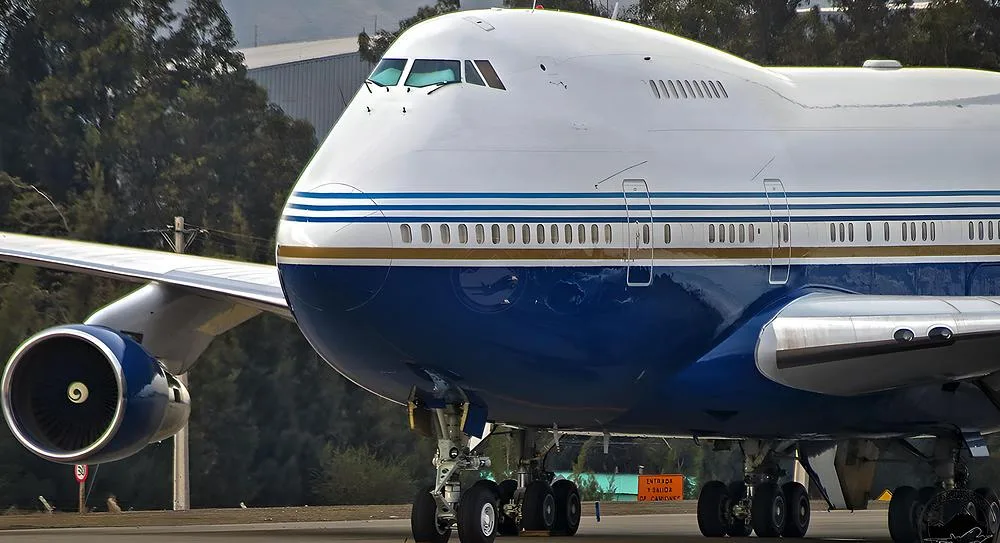 A close-up view of the front section of a Boeing 747 in a blue, white, and gold livery on the tarmac.