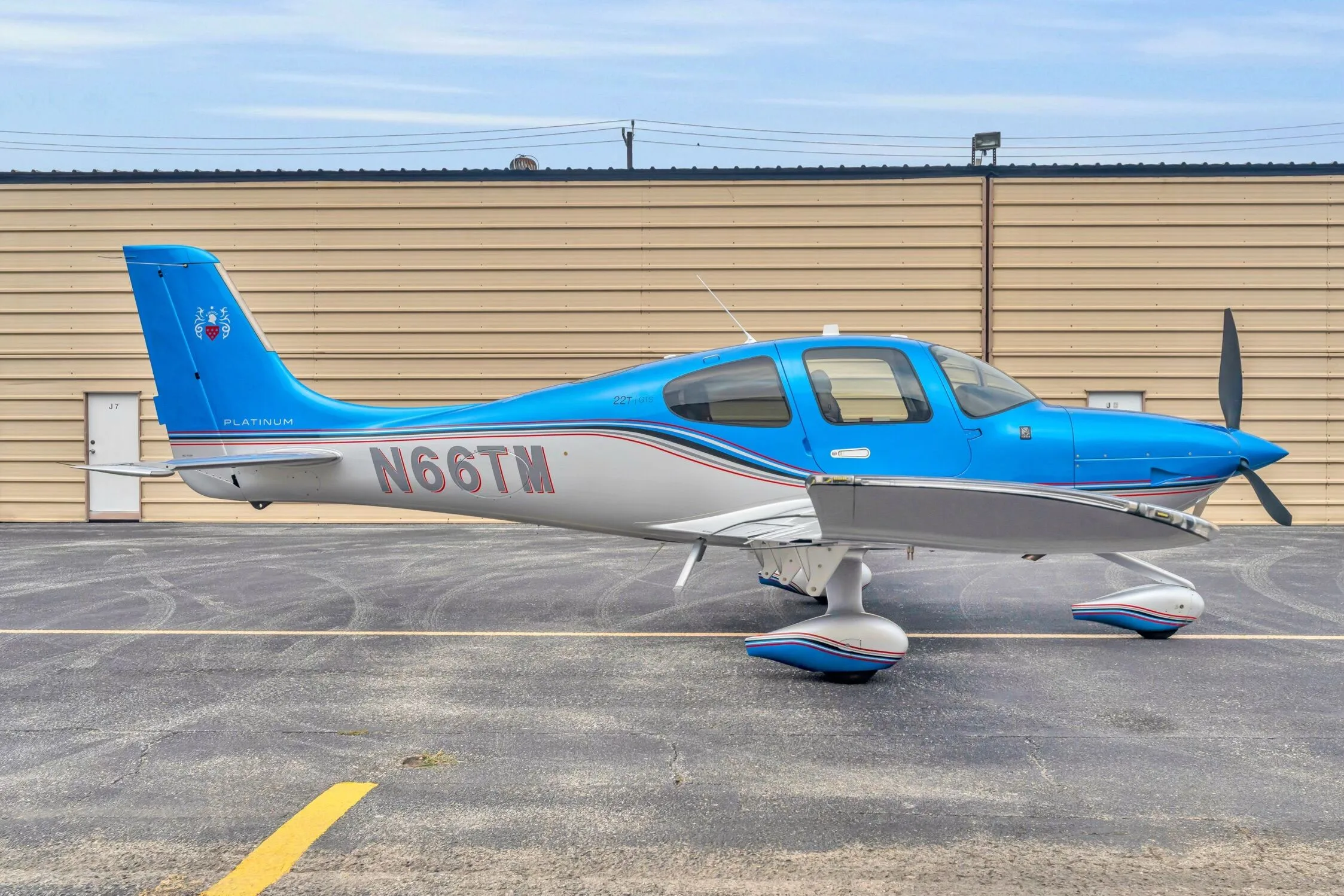 A blue and silver Cirrus SR22T GTS aircraft, registration N66TM, parked on an asphalt ramp next to a hangar.