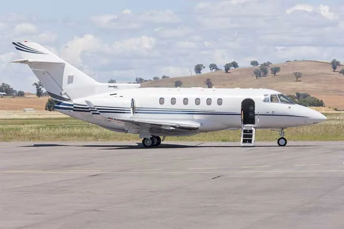 A white Hawker 800XP business jet with blue stripes on an airfield, with its main door open and stairs extended.