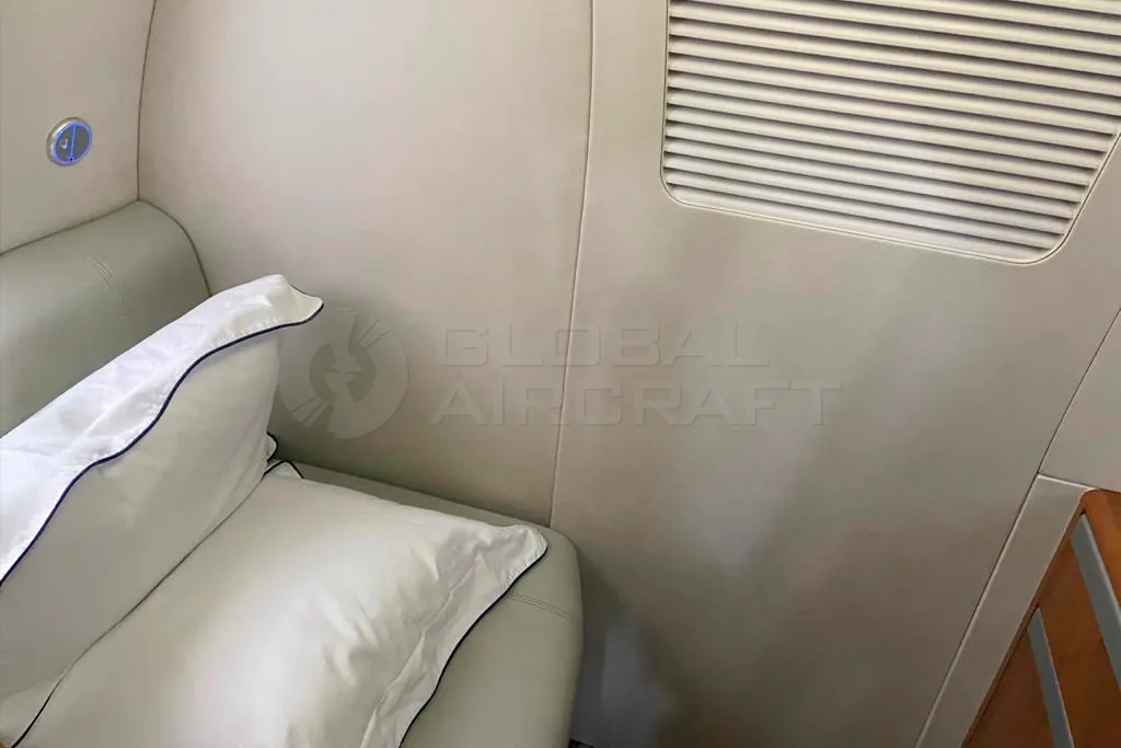 A close-up of an interior seat with white pillows and a light-colored side wall in an aircraft cabin.
