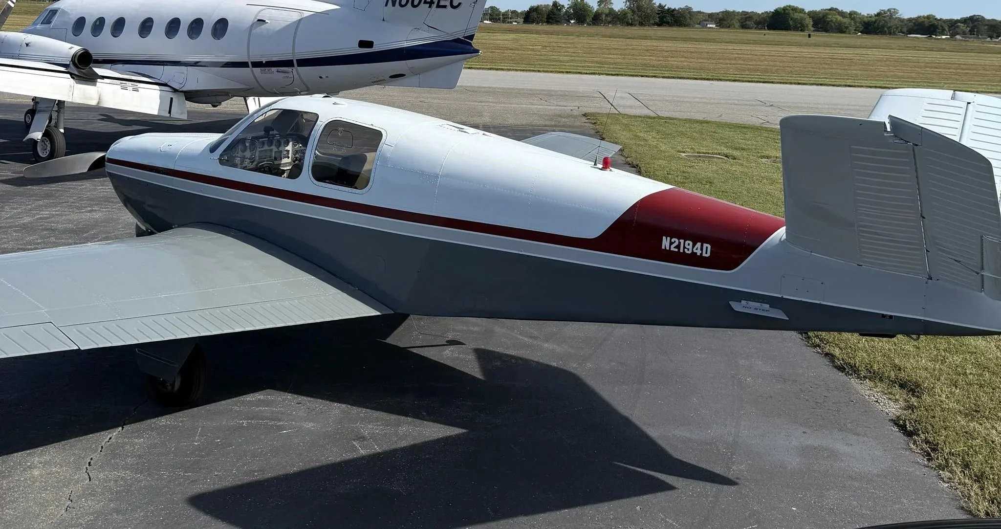 Close-up rear-side view of the N2194D Beechcraft Bonanza V-tail aircraft, showing its white and grey paint scheme with a red stripe.