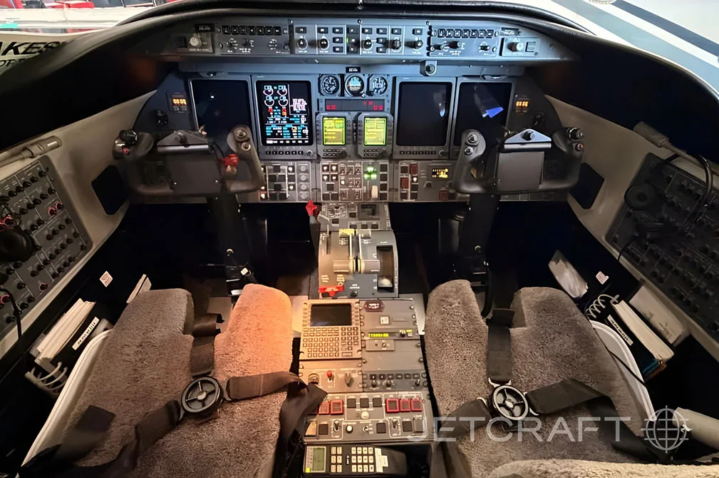 The cockpit of a business jet with multiple display screens and control yokes.