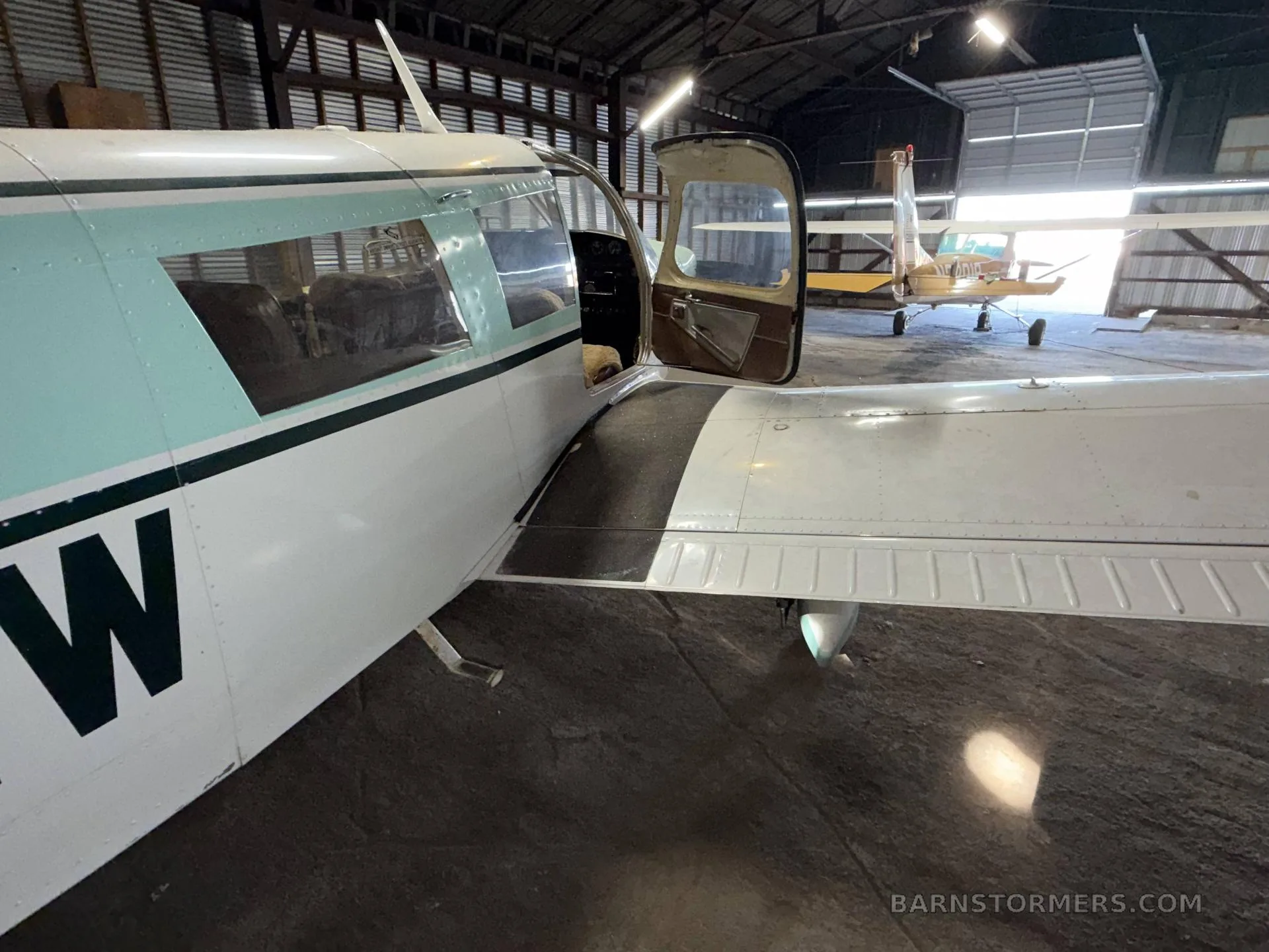 A side view of a white and light green Piper Cherokee Six aircraft (N3391W) with its door open, parked in a hangar.