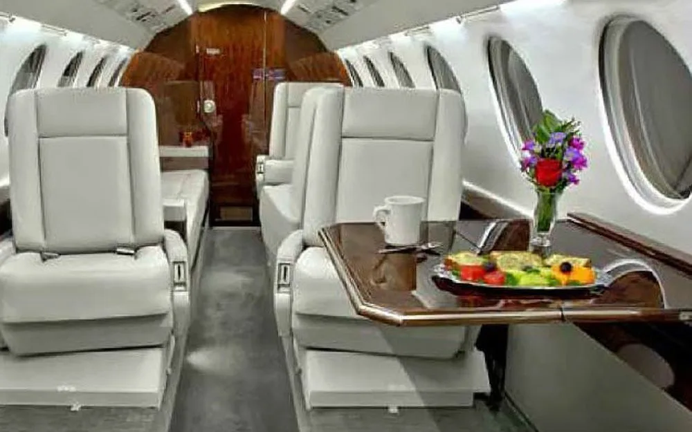 A close-up of the business jet cabin interior with a table set with fruit, a mug, and a vase of flowers.