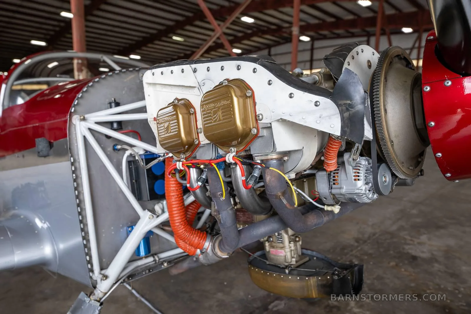 A close-up view of the exposed engine of the red and silver experimental aircraft, showing cylinders and exhaust pipes.