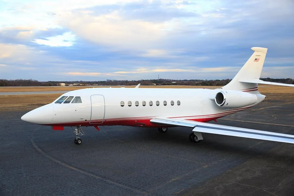 A side view of a white and red Dassault Falcon 900 private jet parked on an airport tarmac.