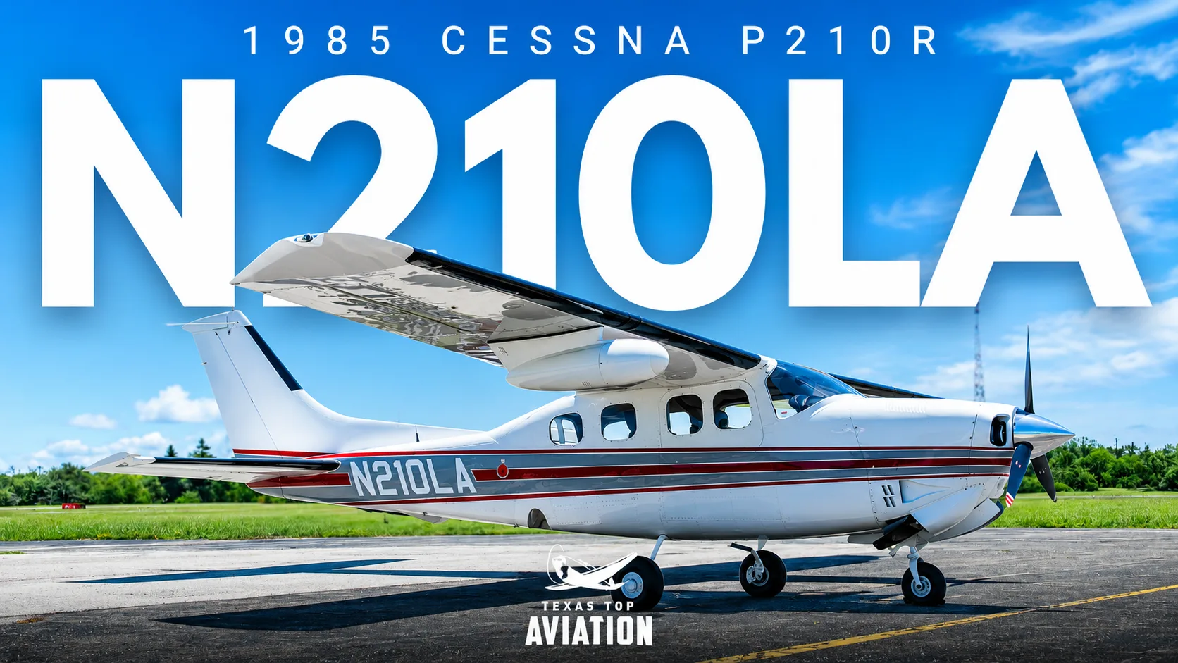 A white 1985 Cessna P210R with red and grey stripes, tail number N210LA, is parked on an asphalt runway under a blue sky.