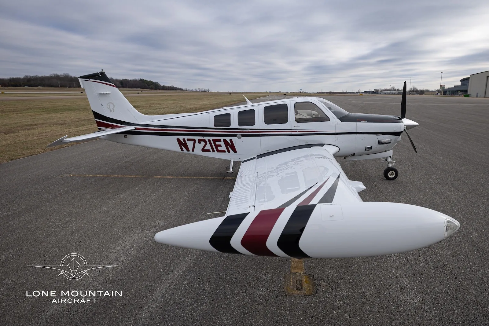 An elevated view of the N721EN single-engine propeller aircraft, highlighting its right wing and wingtip tank with black and red stripes.