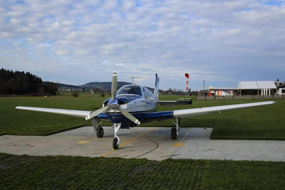 A three-quarter front view of a blue and white single-engine propeller aircraft on a concrete pad under a cloudy sky.
