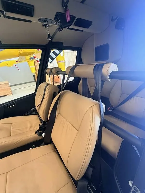 The tan leather interior cabin seats of a helicopter, with a yellow aircraft visible through the window.