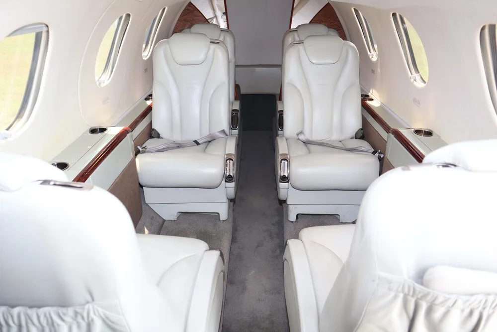 The interior cabin of a private jet, featuring two rows of light cream leather seats facing each other.
