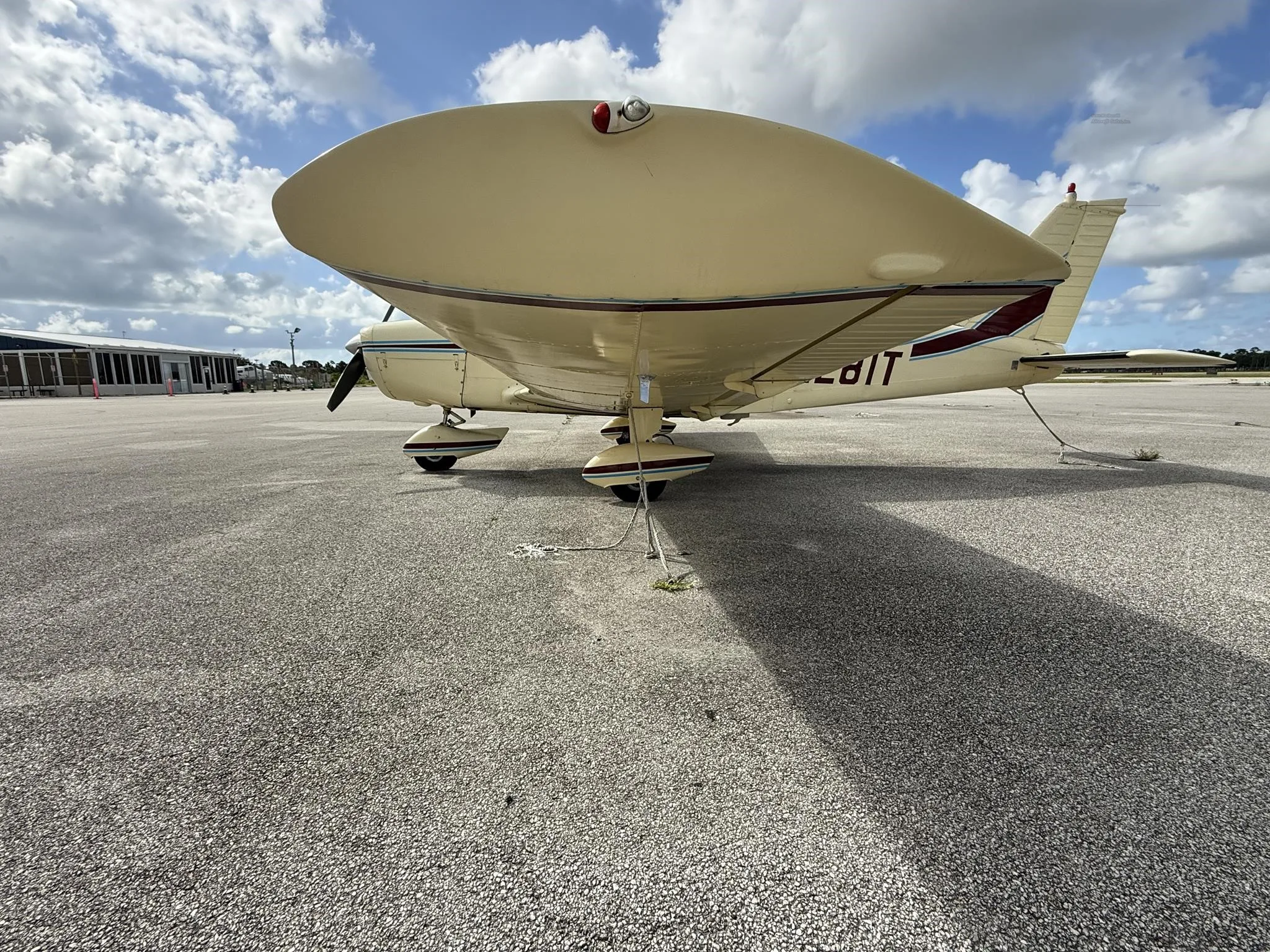 A low-angle view of the underside of a cream-colored Piper PA-28-140E Cherokee, registration N4281T, parked on an airfield.