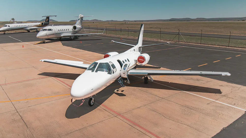 An aerial view of a white Cessna Citation jet with gold and blue stripes parked on an airfield with other private jets.
