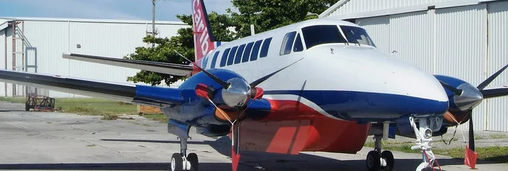 A twin-engine turboprop aircraft with a red, white, and blue paint scheme parked on an airfield.