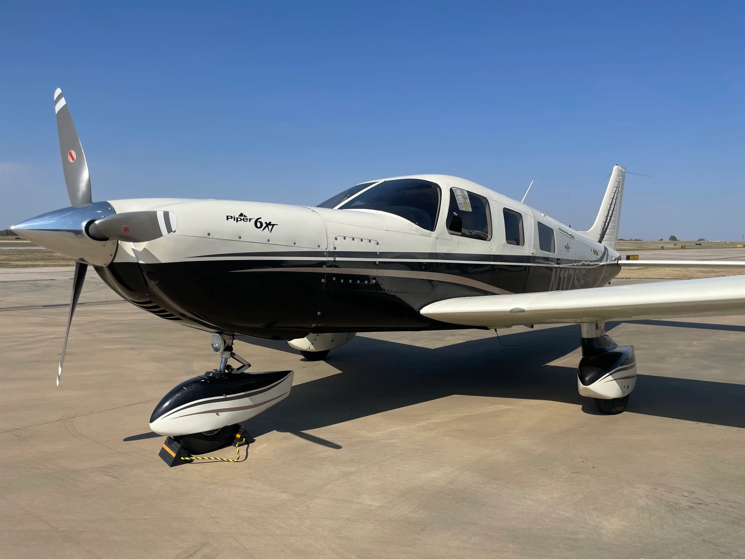 A black and white single-engine propeller aircraft, possibly a Piper M-class, parked on an airfield.
