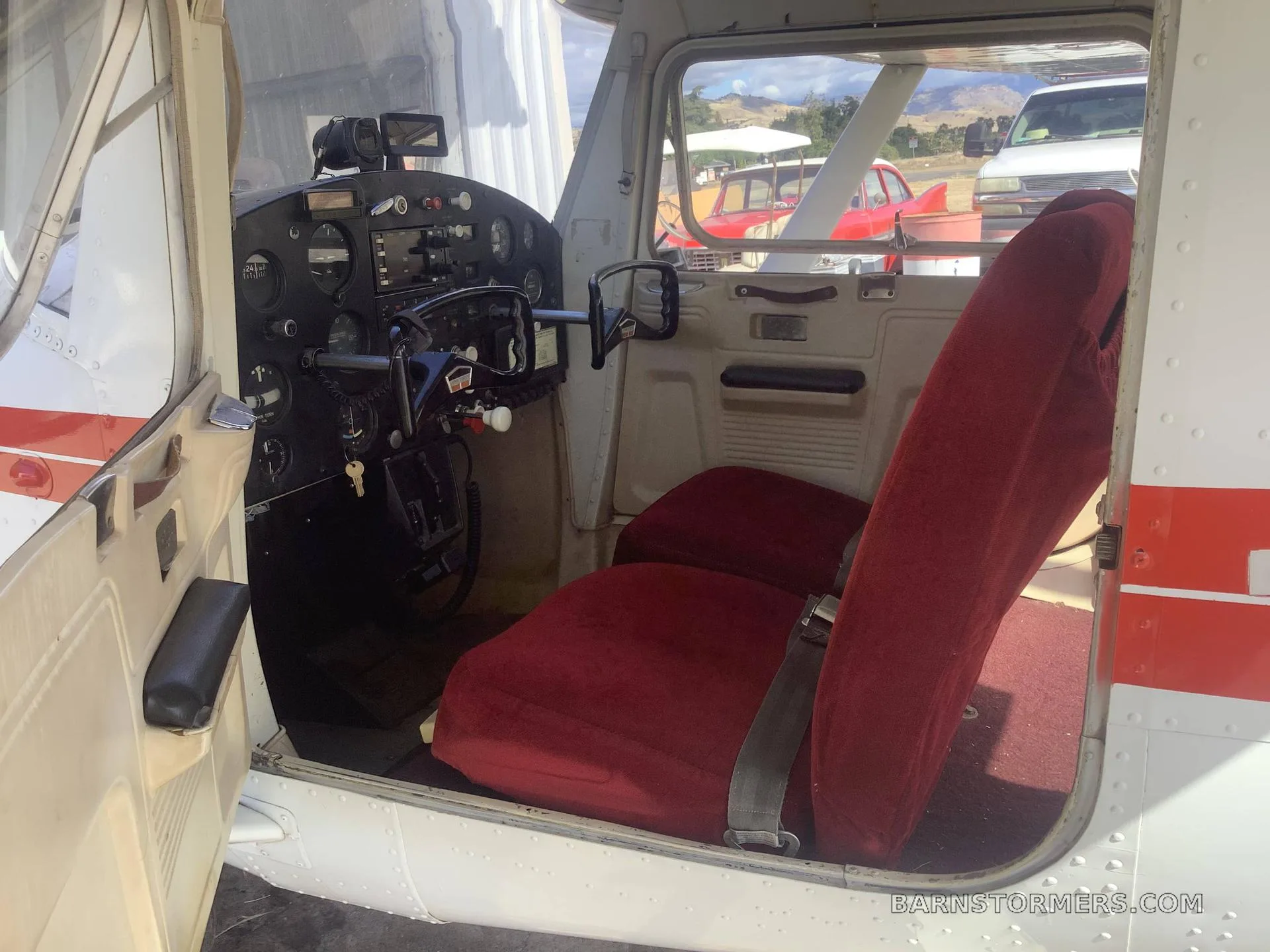 The interior of a small aircraft showing red fabric seats and a partial view of the instrument panel.