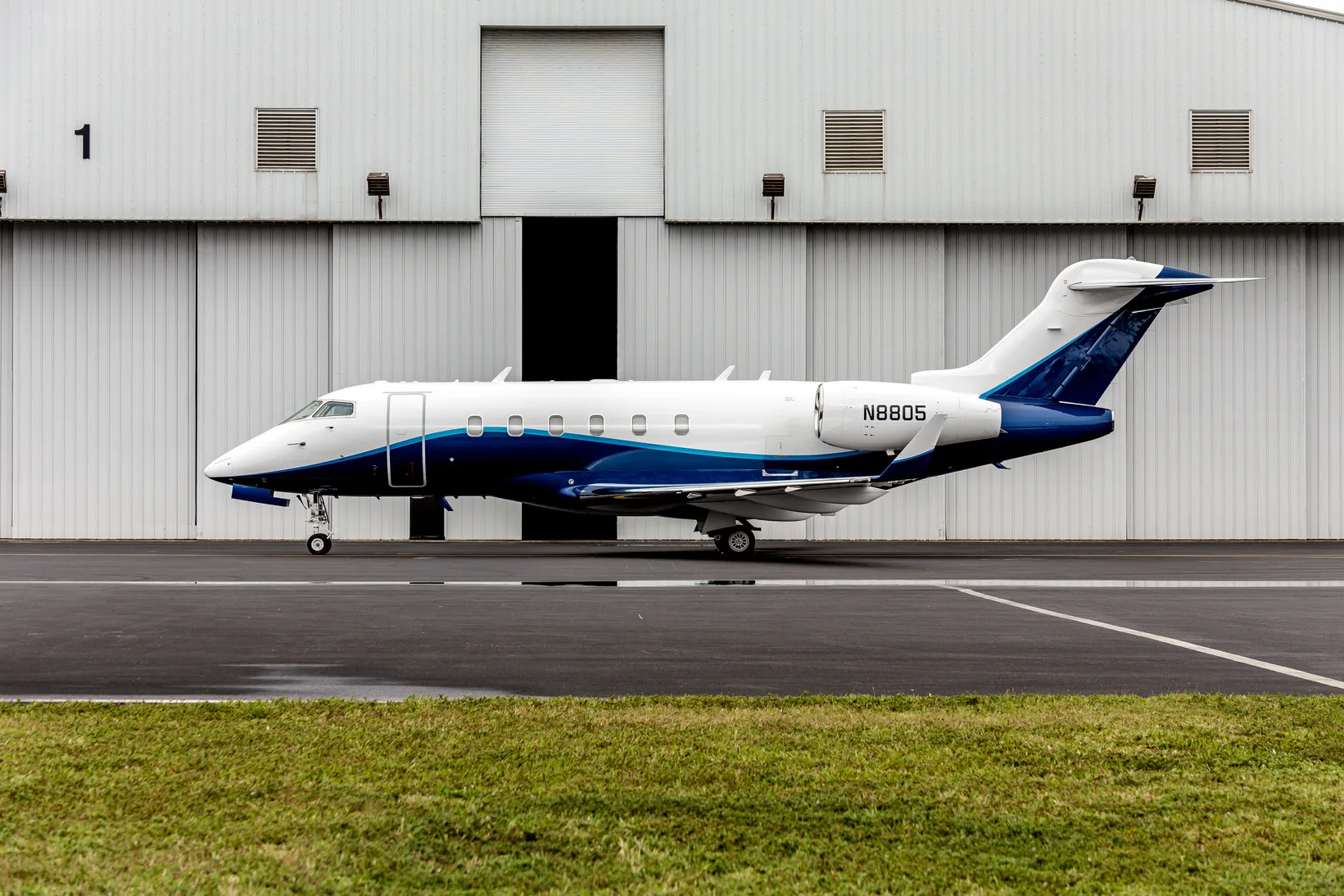 A white and blue private jet, registration N8805, parked on an tarmac in front of a hangar.
