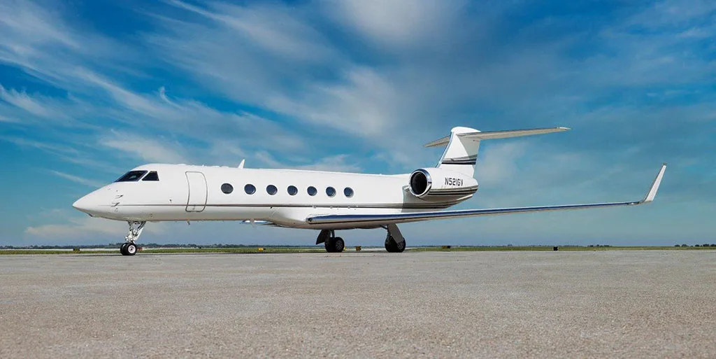 A white Gulfstream G550 business jet, tail number N521GV, parked on a tarmac under a blue sky.