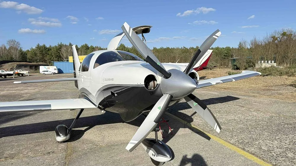 A front view of a white and grey Columbia 400 aircraft with its propeller.