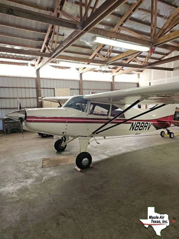 A white single-engine, high-wing aircraft with red stripes and registration N88BRV, parked in a hangar.