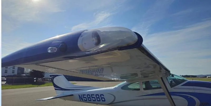 A close-up view of the wing and rear fuselage of the white and blue Cessna N58586 on a sunny day.