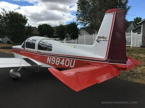 A rear-side view of the white and red Grumman American AA-5 Traveler (N9840U) with its distinctive T-tail.