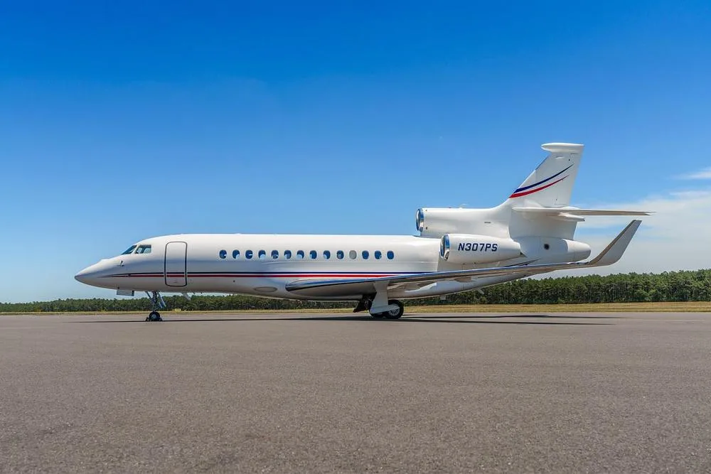 A side view of a white Dassault Falcon 900EX business jet with red and blue accents, parked on an airfield.