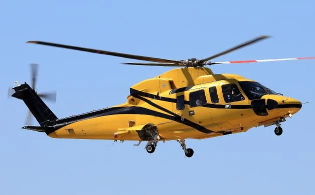 A yellow helicopter with black stripes flies against a clear blue sky.