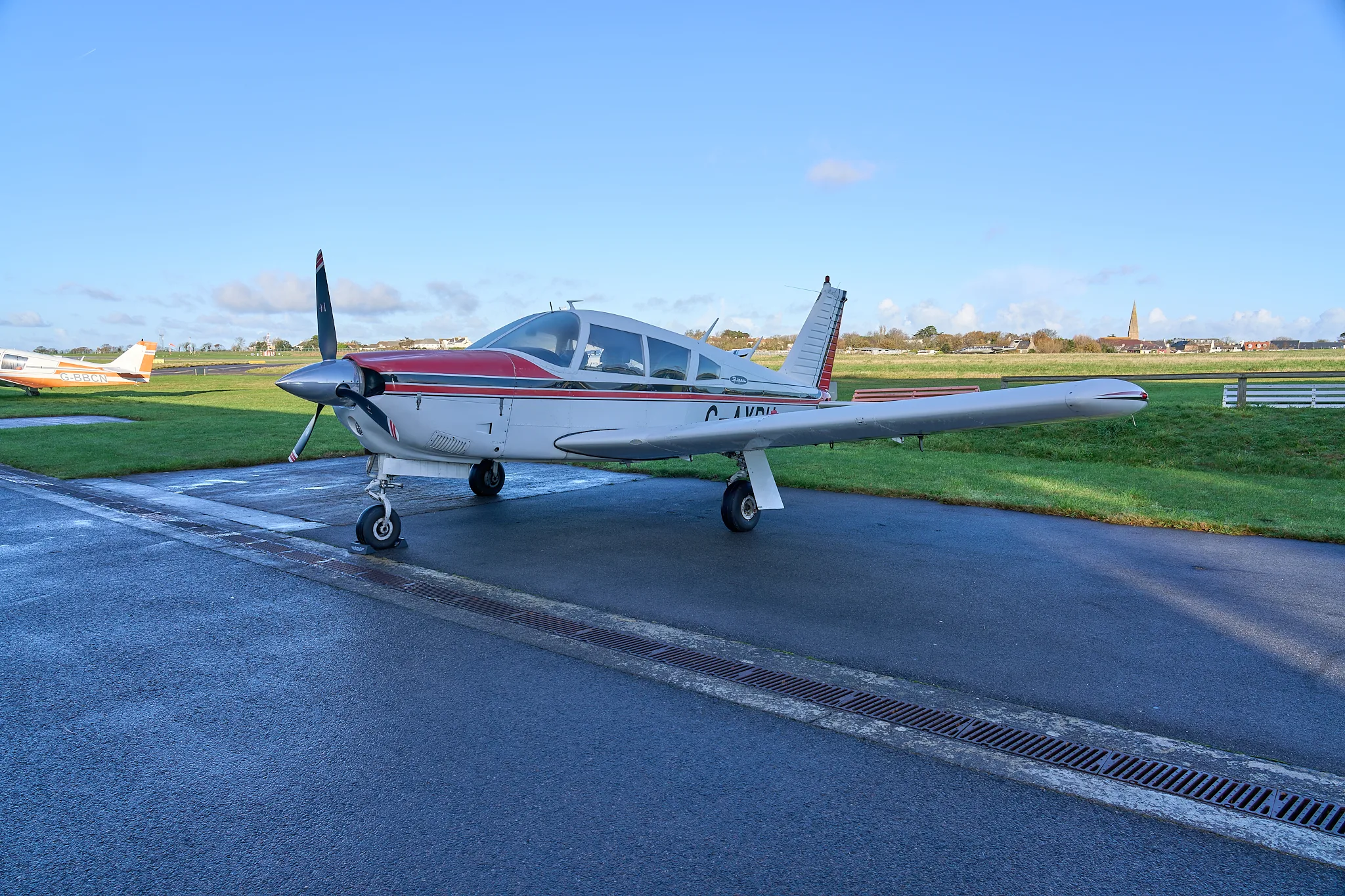 A white and red Piper Cherokee G-AYPU parked on a wet tarmac at an airfield.