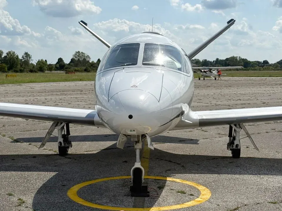 A head-on view of a white Cirrus Vision Jet parked on an airfield with a yellow circle marking.