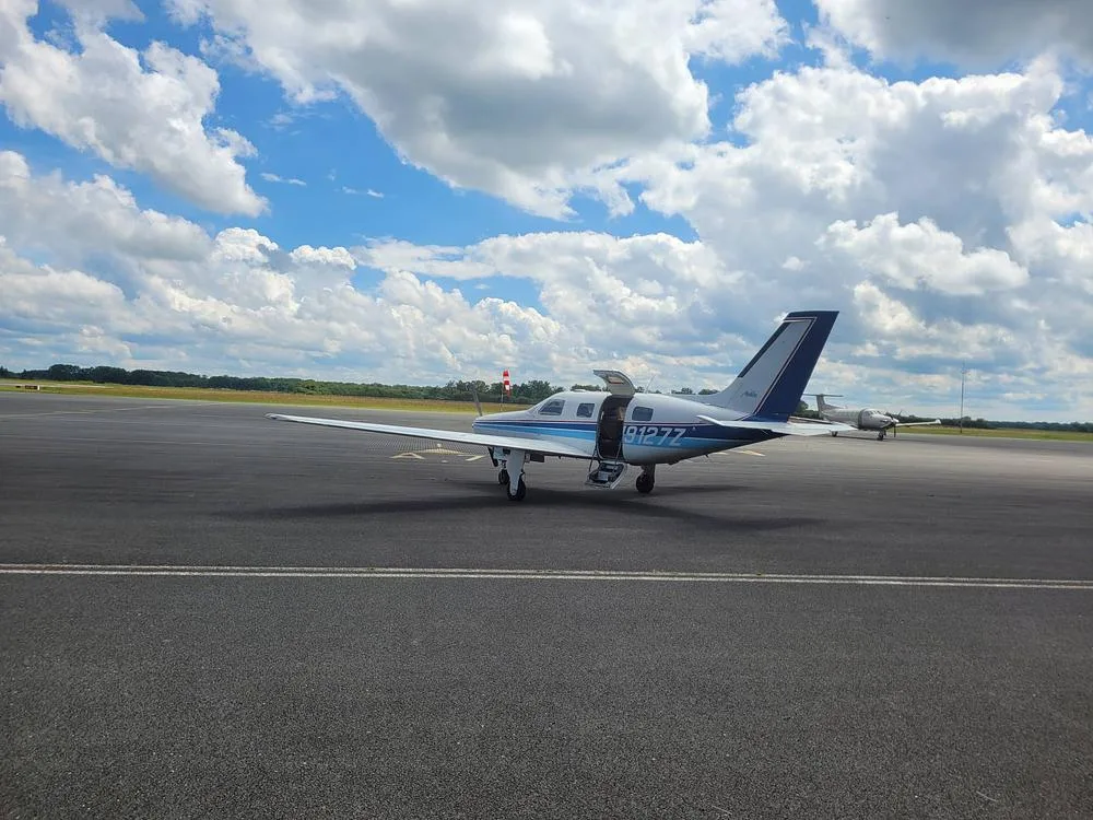 A white and blue Piper PA-46-350P Malibu Mirage aircraft, registration N9127Z, parked on an asphalt runway under a partly cloudy sky.
