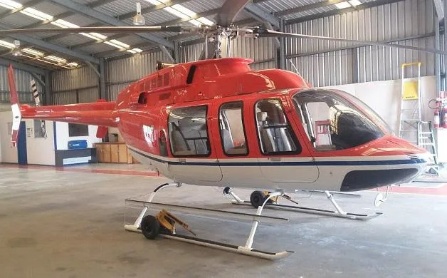 A red and white helicopter with blue stripes on its belly, parked inside a hangar.