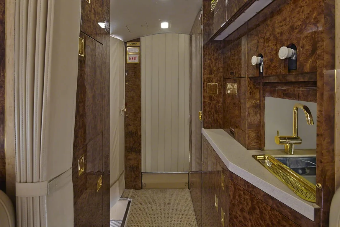 A private jet galley area with polished wood cabinetry, a gold faucet, and a curtained entryway.