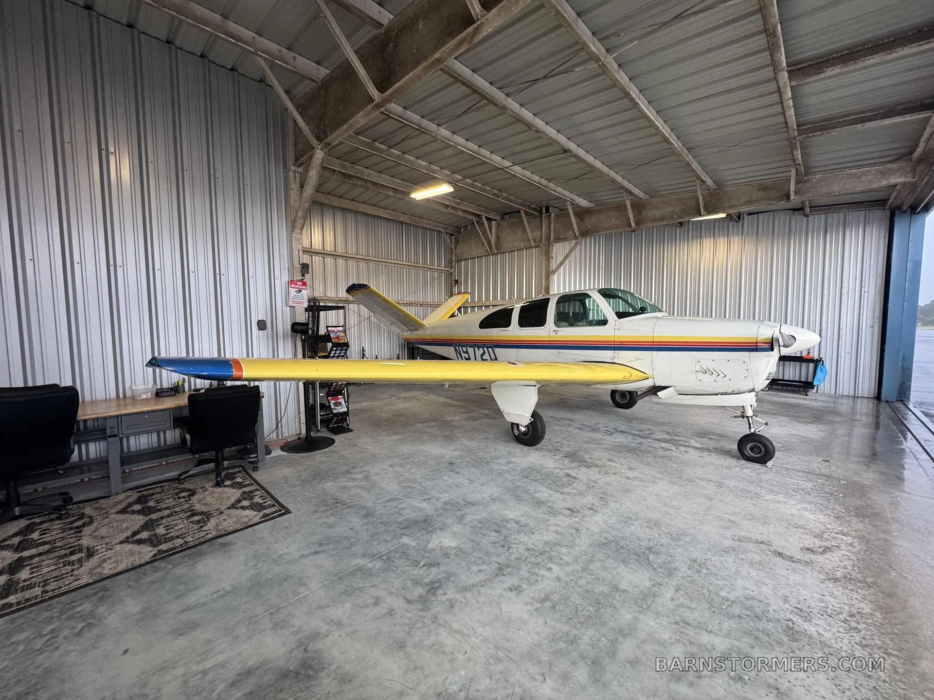 A white and yellow single-engine aircraft with rainbow stripes on the fuselage, parked inside a metal hangar.