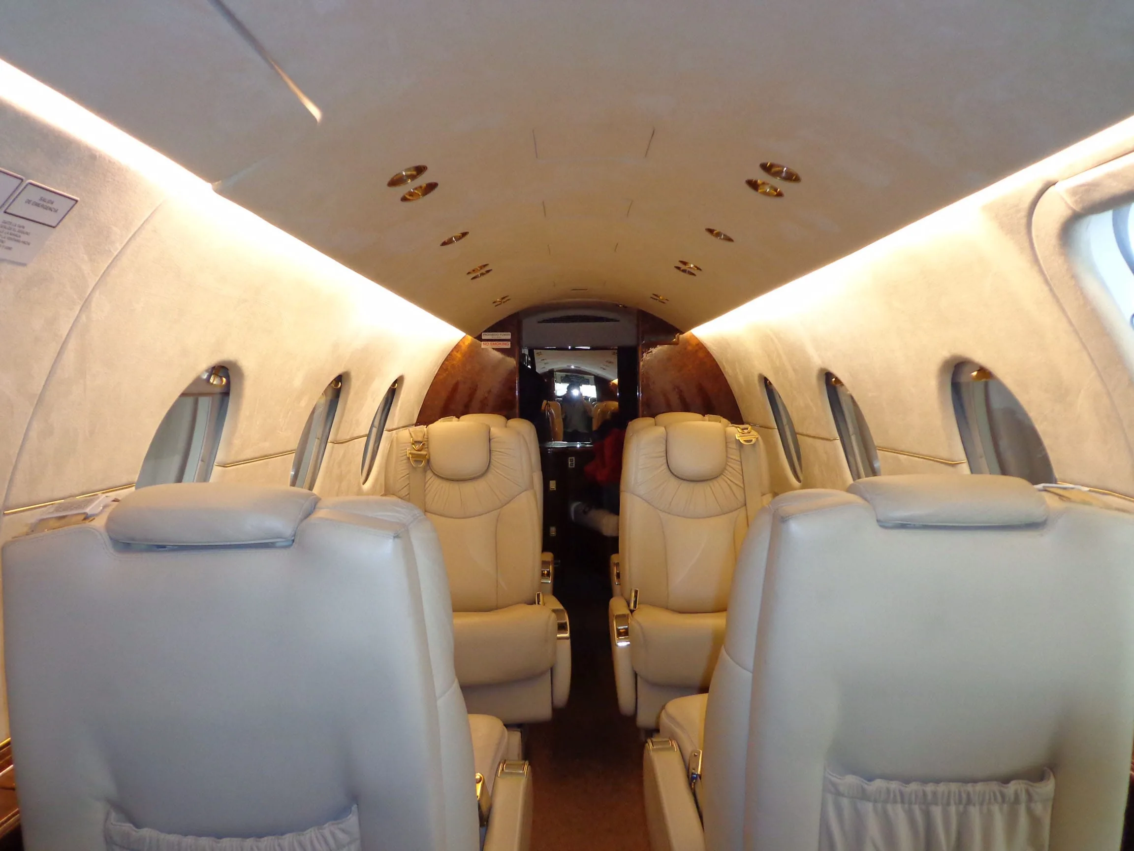 The interior cabin of a private jet with light beige leather seats and warm overhead lighting.