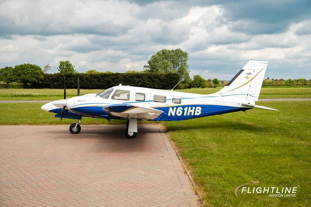 A side view of the N61HB Piper Seneca aircraft, white with blue and gold accents, parked on a tarmac.