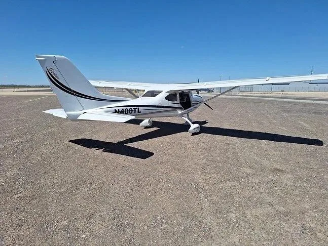A rear three-quarter view of a white Sirius LightSport aircraft with black and grey stripes, registration N400TL, parked on an airfield.