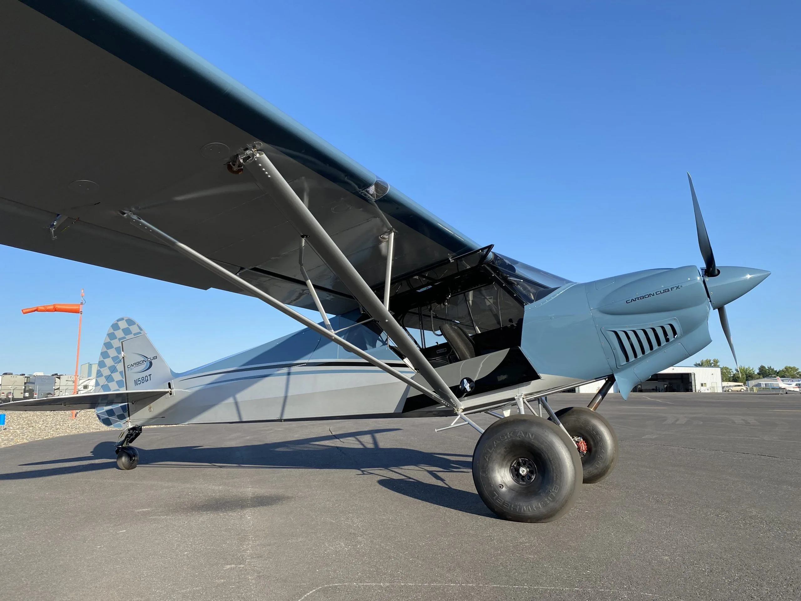 A side view of a blue and grey Carbon Cub FX-3 aircraft with registration N58QT parked on a tarmac.