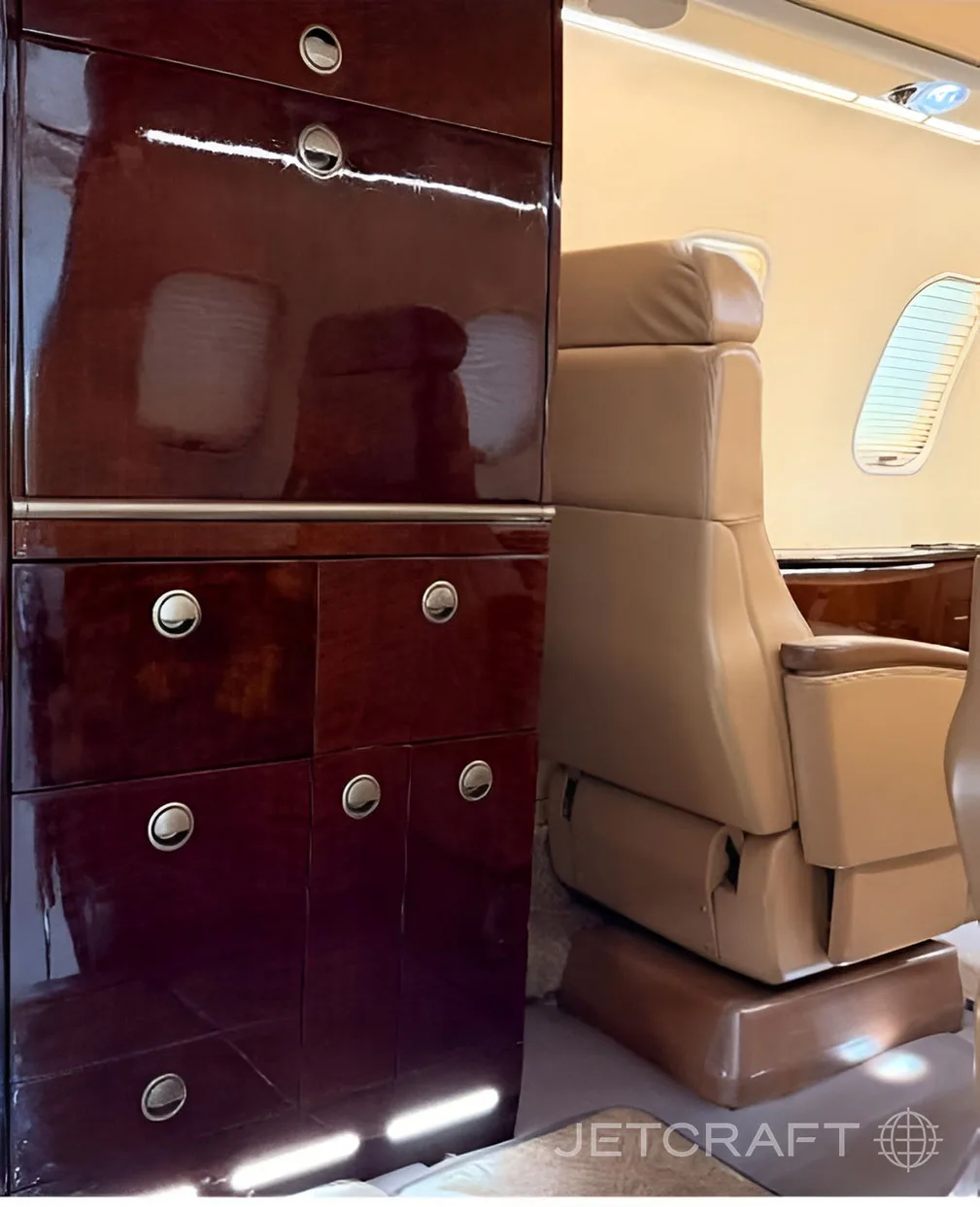 A close-up of a dark wood cabinet and a tan leather seat in a business jet cabin.