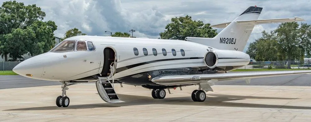 A white and black Hawker 800XP business jet with tail number N920EJ is parked on a tarmac with its main door open.