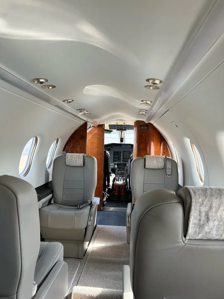 A view down the aircraft's interior cabin aisle, showing grey seats and the cockpit entrance with wood accents.